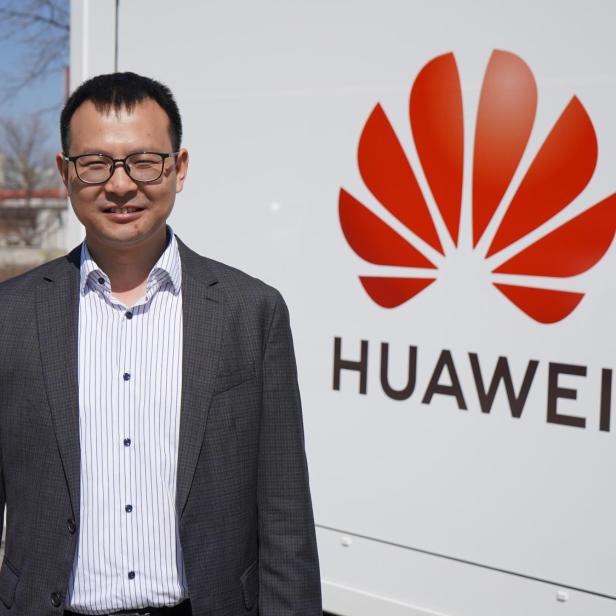 Ein asiatischer Mann steht vor dem Logo von HUAWEI.