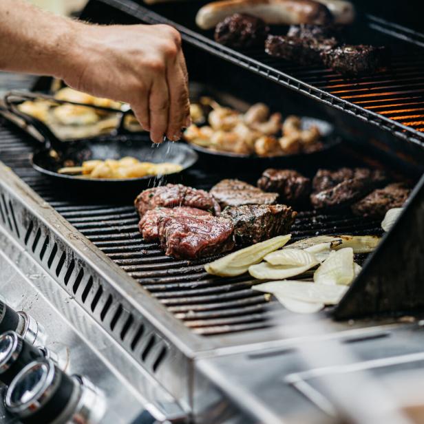 Ein Koch würzt Steaks und Zwiebeln auf einem Grill.