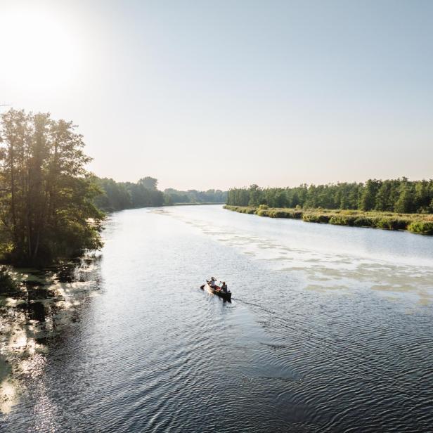 Ein Kanu auf einem breiten Fluss inmitten der Natur im Sonnenuntergang. 