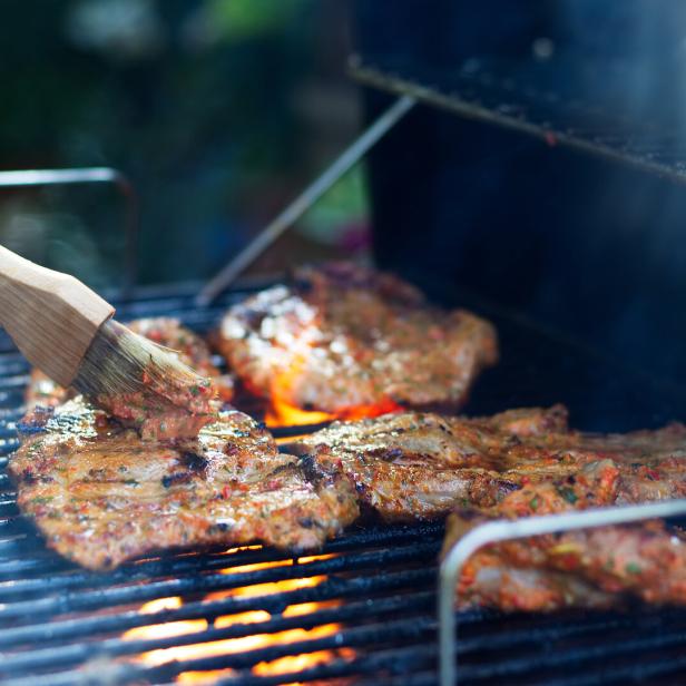 Mit einem Pinsel wird Fleisch auf einem Grill mariniert.