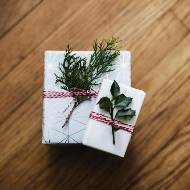 Zwei eingepackte Geschenke unterschiedlicher Größe, die übereinander liegen und jeweils ein Pflanzenblatt drauf liegt. 