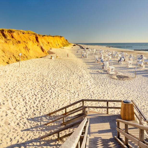 Ein weißer Strand mit Strandkörben und einer Klippe hintendran. 