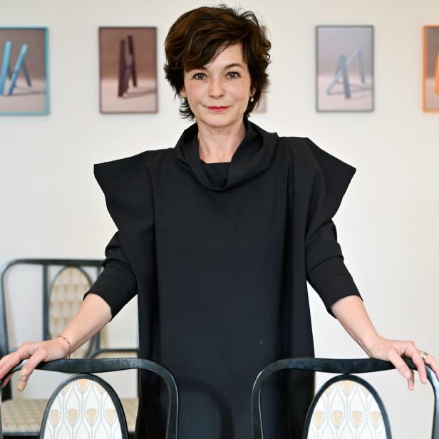 Eine Frau in einem schwarzen Kleid posiert vor einer Wand mit abstrakten Bildern.