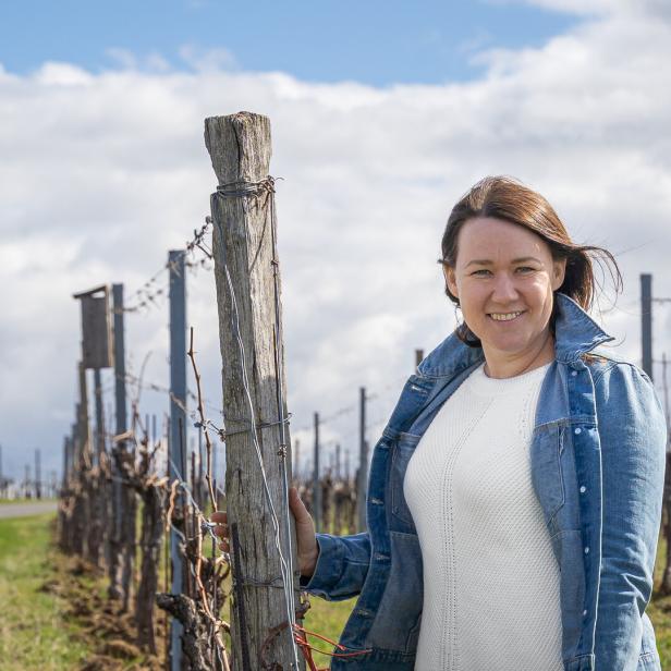 Eine Frau lächelt in einem Weinberg, während der Wind durch ihr Haar weht.