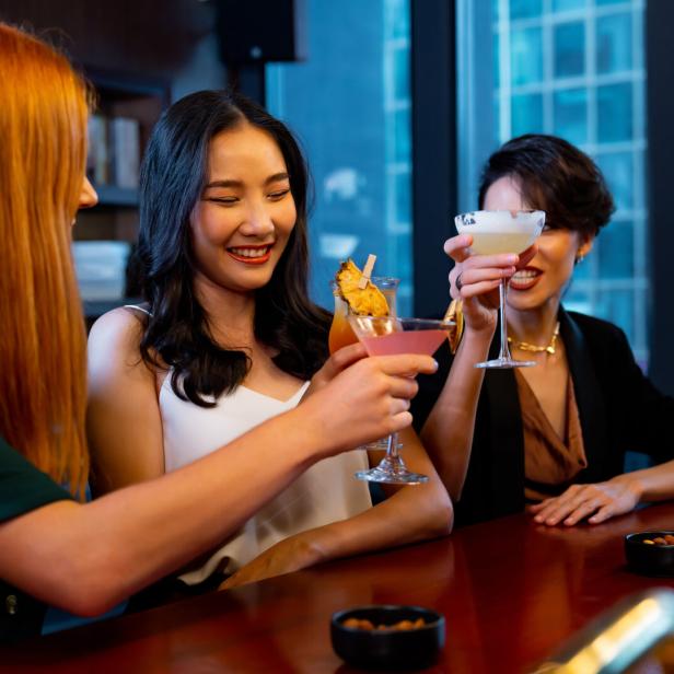 Eine Gruppe von jungen Frauen stößt mit Cocktails an der Hotelbar an.