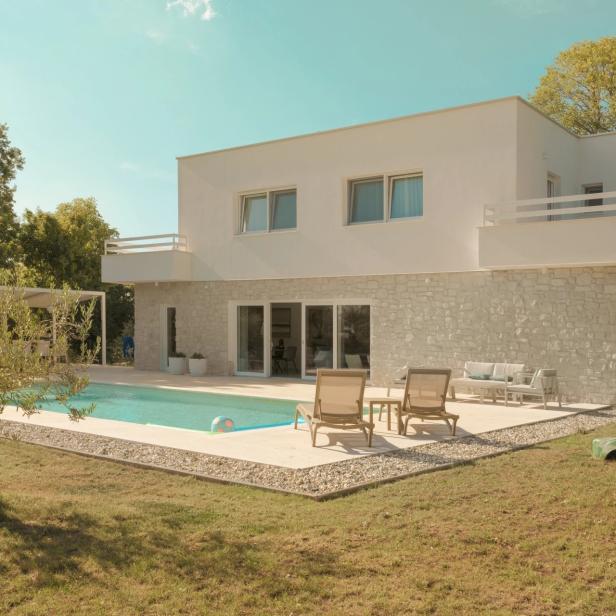 Ein Gebäude von außen, weiß, mit Pool, Liegestühlen und Garten