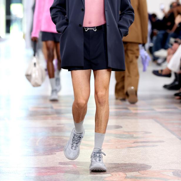 Ein Mann in Shorts, Blazer und Turnschuhen läuft auf einem Laufsteg.