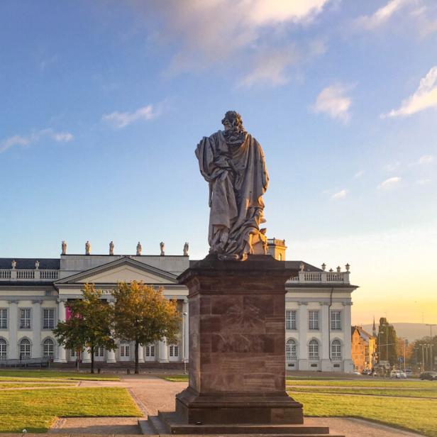 Statue eines Mannes vor einem Gebäude, das die architektonische Schönheit der Umgebung betont.