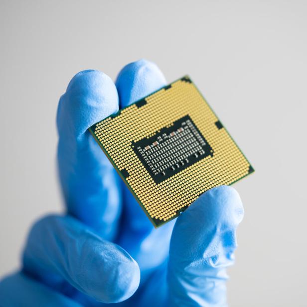 Behandschuhte Hand hält ein Elektronikbauteil mit Goldkontakten