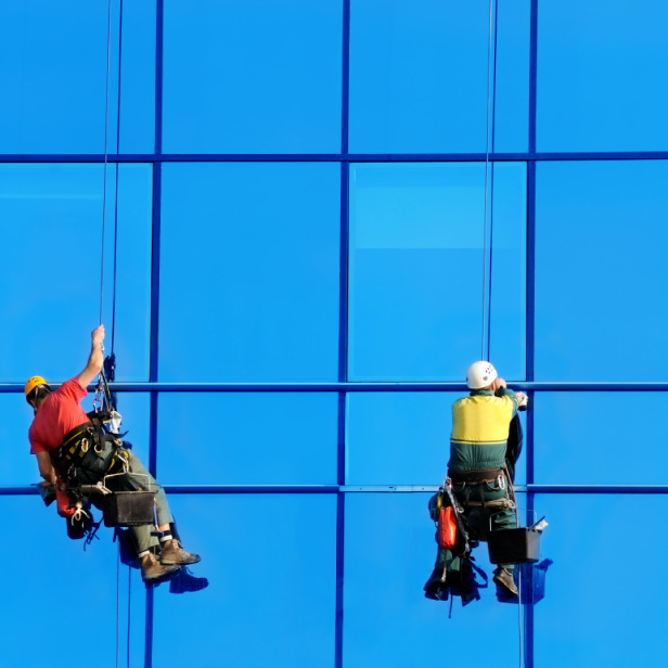 Zwei Fensterputzer hängen an der Fassade eines Hochhauses. 