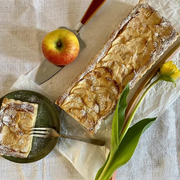 Ein Apfel-Rhabarber-Kuchen neben einer gelben Blume und einem Apfel.