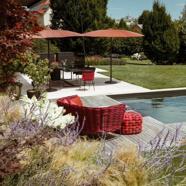 Ein Garten mit Pool, Terrasse, roten Gartenmöbeln und üppiger Bepflanzung.