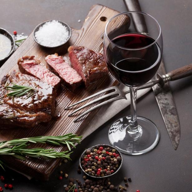 Ein Steak, tranchiert auf einem Holzbrett, mit einem Glas Rotwein und Gewürzen angerichtet.