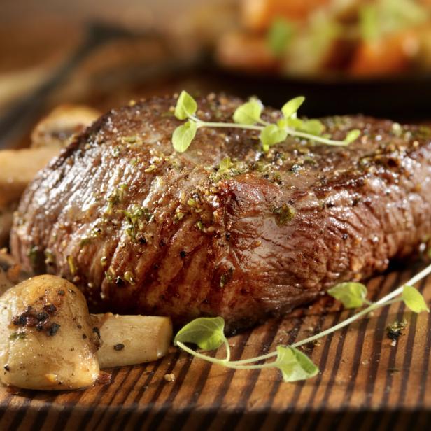Ein saftiges Steak mit Pilzen auf einem Holzbrett angerichtet.
