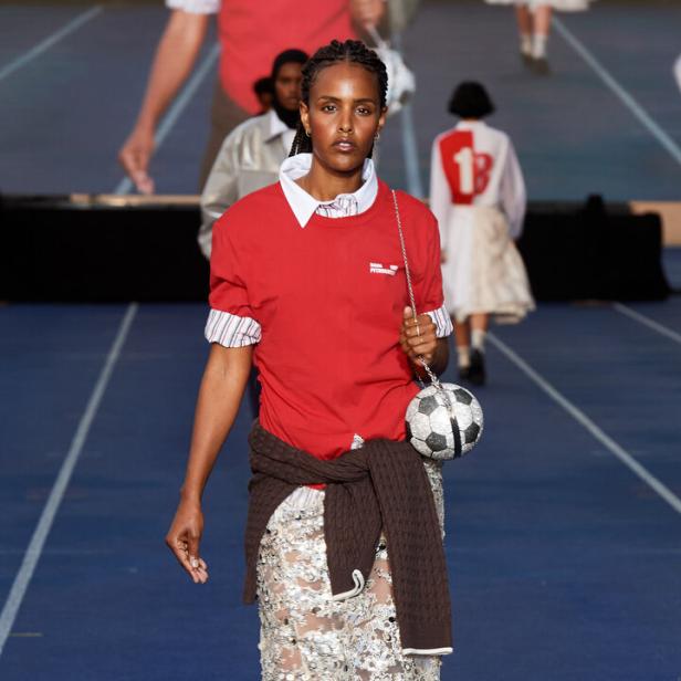 Eine Frau in Sportkleidung mit einer Handtasche in Form eines Fußballs auf einem Laufsteg.