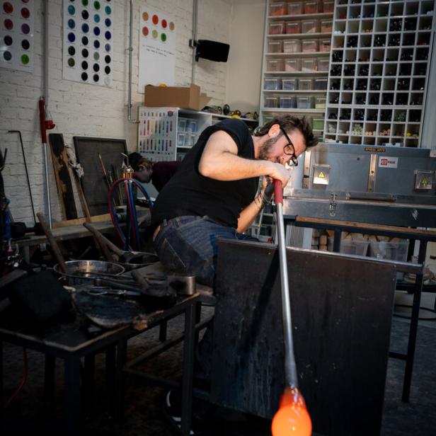 Ein Glasbläser formt in seiner Werkstatt eine glühende, orangefarbene Glasmasse.