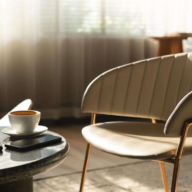 Eine Tasse Kaffee, ein Notizbuch und ein Smartphone auf einem Tisch neben einem Sessel.