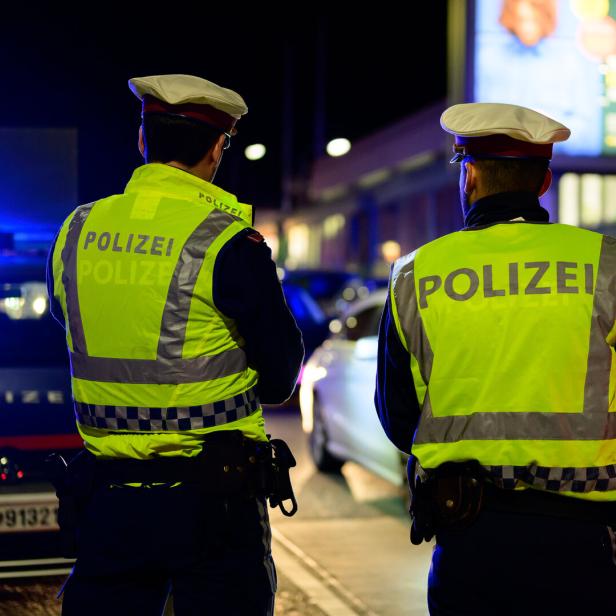 Polizisten stehen nachts vor ihren Polizeiautos.