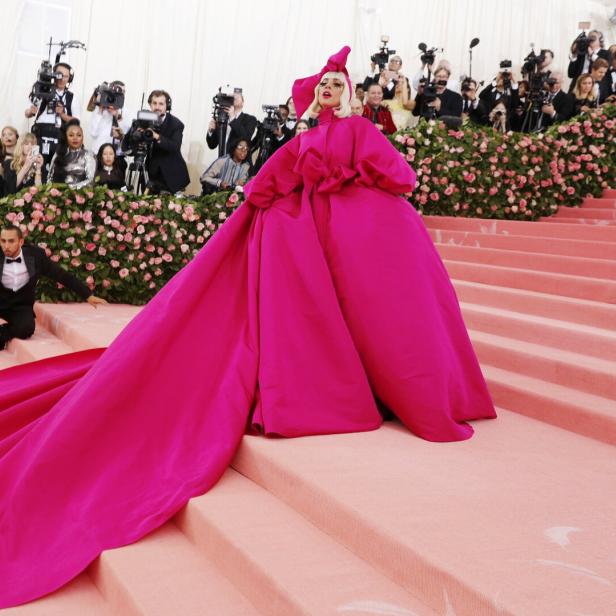 Lady Gaga in einem pinkfarbenen Kleid mit Schleppe auf dem roten Teppich, umgeben von Fotografen.
