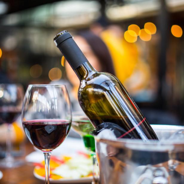 Eine Flasche Rotwein in einem Eiskühler und ein Glas Rotwein auf einem Tisch.