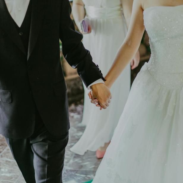 Frau im weißen Brautkleid Hand in Hand mit Mann im schwarzen Anzug