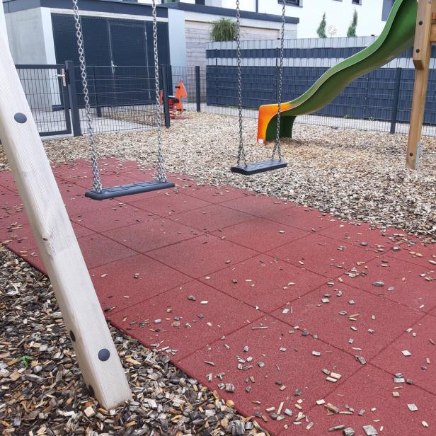Ein Spielplatz mit Schaukeln, einer Rutsche und einem roten Gummiboden.