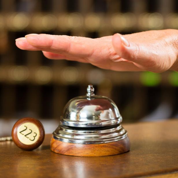 Eine Hand kurz vor dem Läuten einer Hotelglocke an der Rezeption.