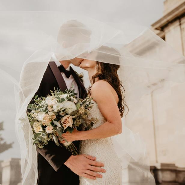 Hochzeitspaar küsst sich unter Brautschleier.