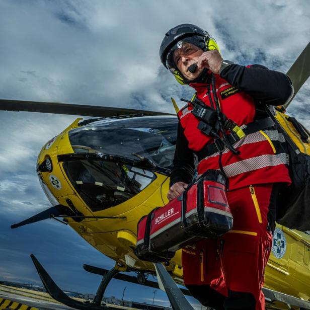 Ein Mann in roter und gelber Kleidung steht neben einem Hubschrauber.
