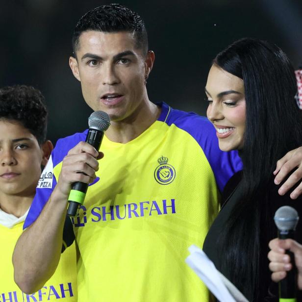 Cristiano Ronaldo spricht mit einem Mikrofon, während Georgina Rodríguez lächelt.