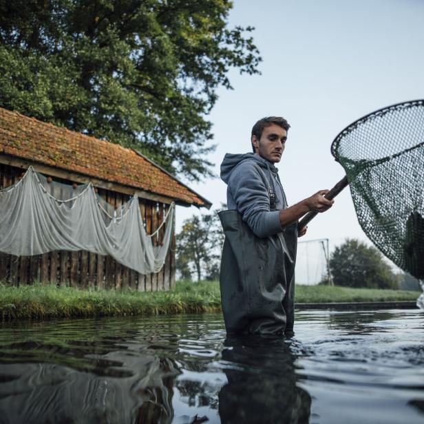 Ein Fischer steht im Wasser und hält ein Netz mit einem Fisch darin.