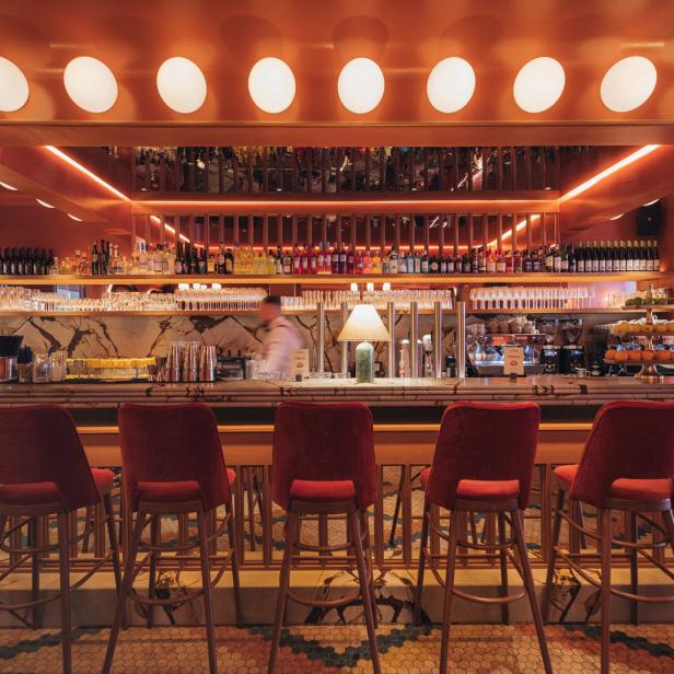Eine Bar mit roten Samtstühlen und einer beleuchteten Theke voller Getränke.