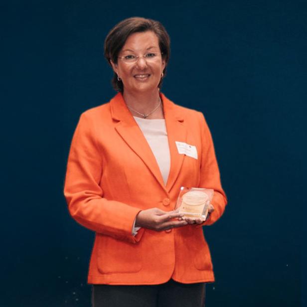Eine Frau in einem orangenen Blazer vor einer schwarzen Wand