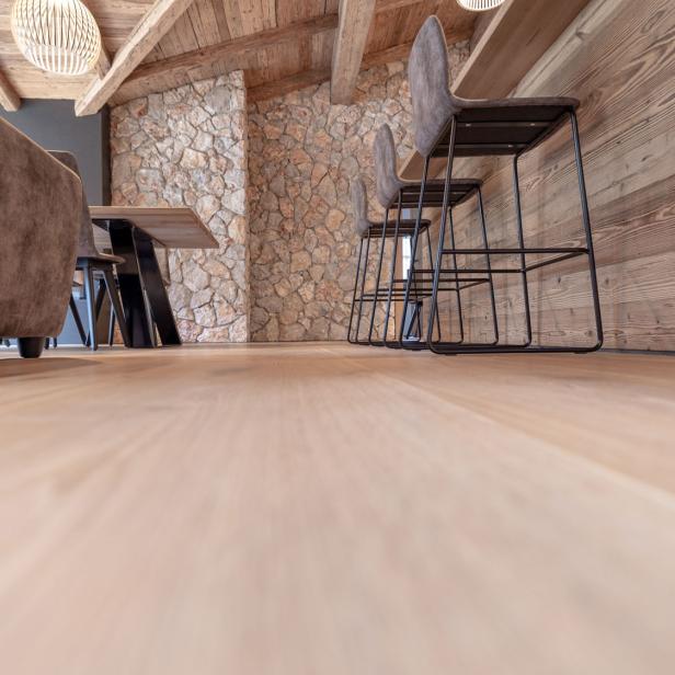 Ein Holzboden, weiter hinten sind Holzstühle zu sehen. 