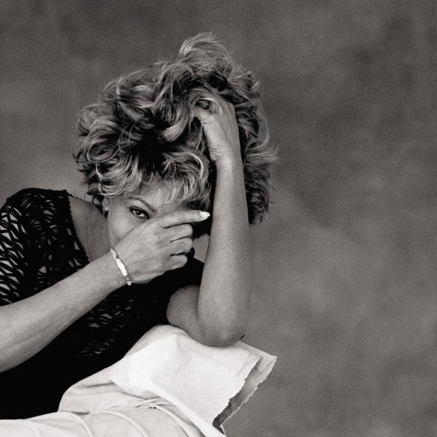 Tina Turner, fotografiert von Peter Lindbergh, blickt mit einer Hand vor dem Gesicht in die Kamera.