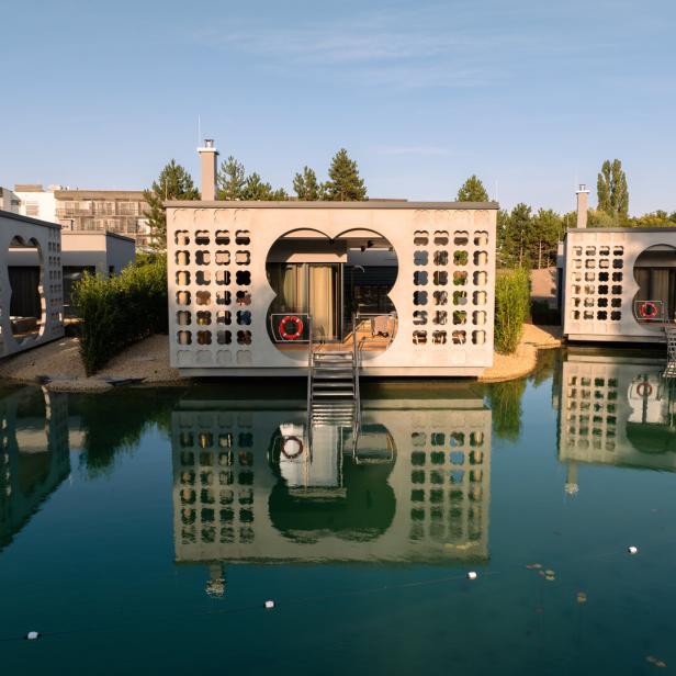Moderne schwimmende Häuser mit dekorativen Fassaden spiegeln sich im Wasser.