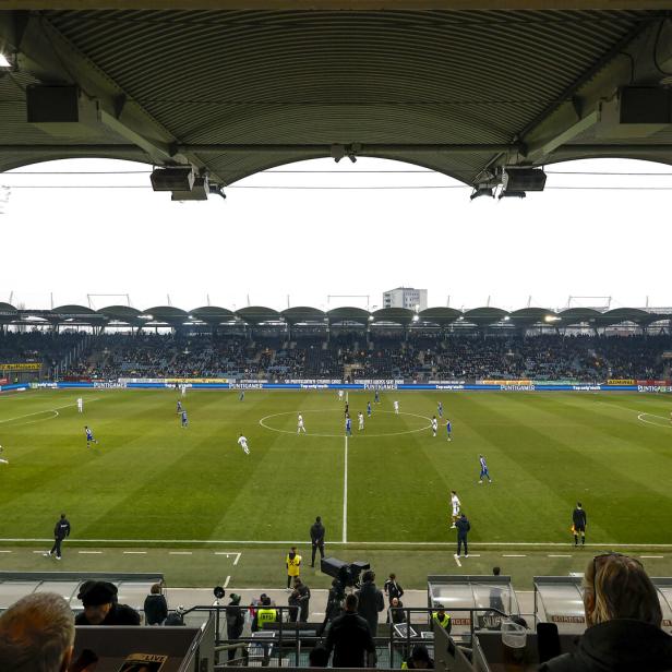Blick von der Tribüne auf ein Fußballspiel in einem Stadion mit Zuschauern.