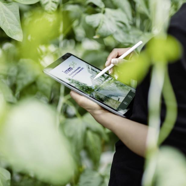 Eine Frau steht mit einem Tablet im Grünen. 