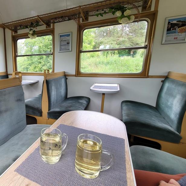 Ein Speisewagen in eine Zug; vorne im Bild ist ein Tisch mit zwei Gläsern Weißwein zu sehen.