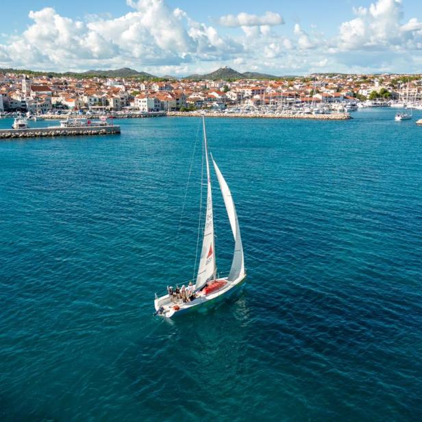 Luftaufnahme eines Segelbootes im Meer mit der Stadt Vodice im Hintergrund.