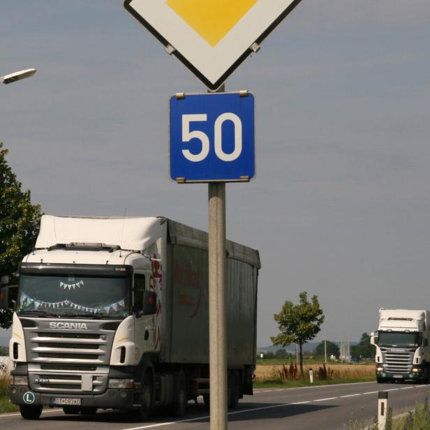 Straßenschild mit Vorfahrt und Tempo 50, daneben zwei Lastwagen auf einer Landstraße.