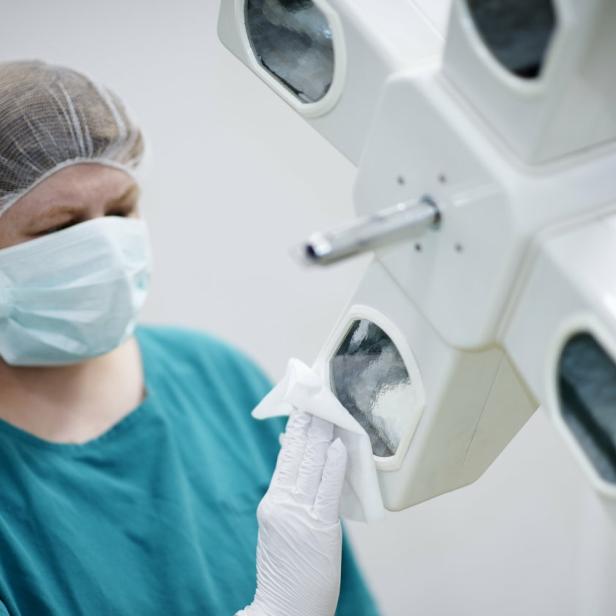 Eine Frau in einem OP-Mundschutz und Scrub-Anzug hält ein chirurgisches Licht.