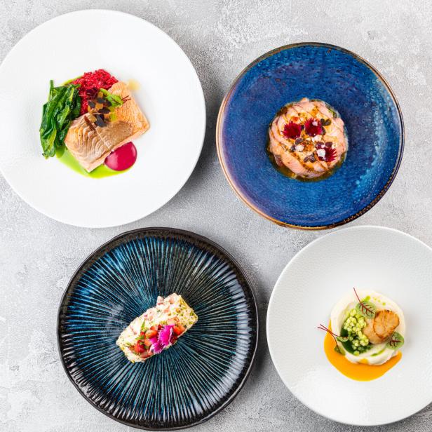 Vier Teller mit kunstvoll angerichteten Speisen, darunter Fisch und Meeresfrüchte.