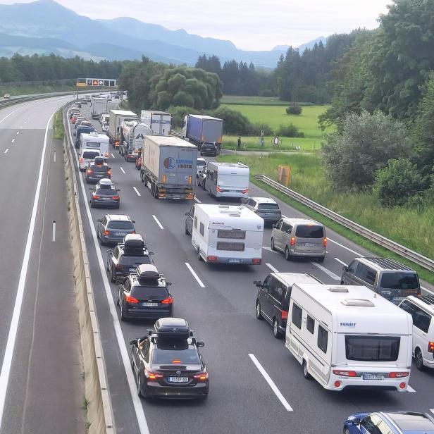 Stau auf der Autobahn mit vielen Autos und Lkw vor grüner Bergkulisse.