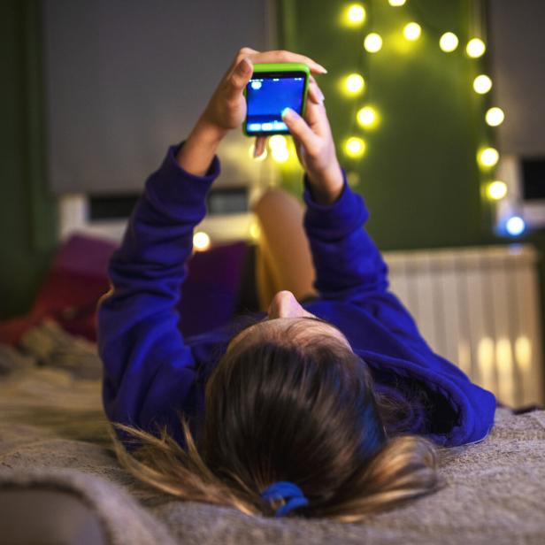 Ein Mädchen schaut auf ihr Smartphone, während es im Bett liegt.