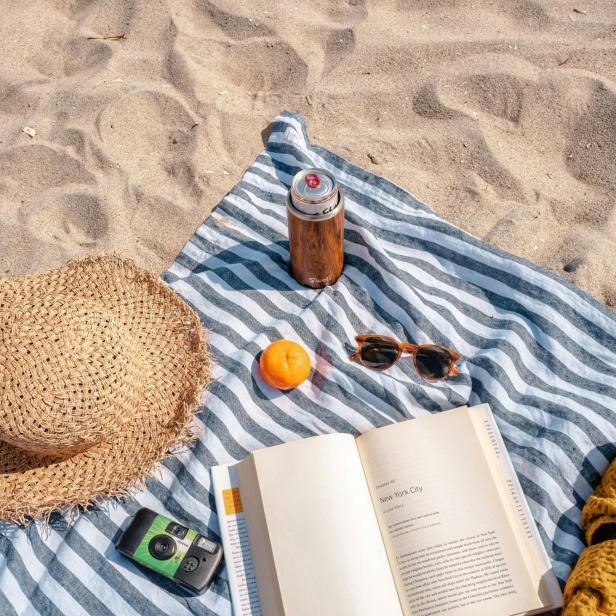Ein Strandtuch mit einem Sonnenhut, einem Buch, einer Kamera und einer Sonnenbrille, am Strand