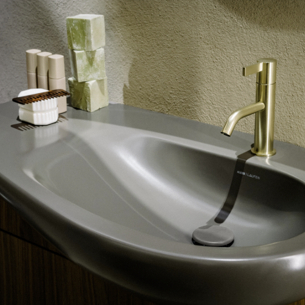 Ein schwarzes Waschbecken von LAUFEN mit einem goldenen LAUFEN-Wasserhahn. 