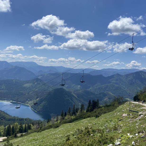 Bergausblick auf einen im Tal liegenden See mit grüner Hügellandschaft im Hintergrund.