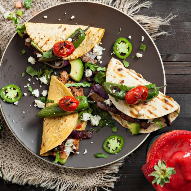 Drei Tacos mit gegrilltem Gemüse und Fleisch auf einem Teller, dazu Margaritas.