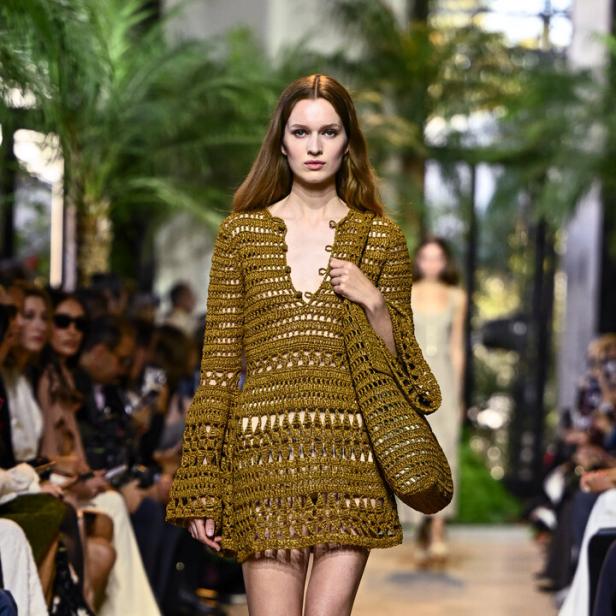 Ein Model läuft auf dem Laufsteg in einem gehäkelten Minikleid mit passender Tasche.